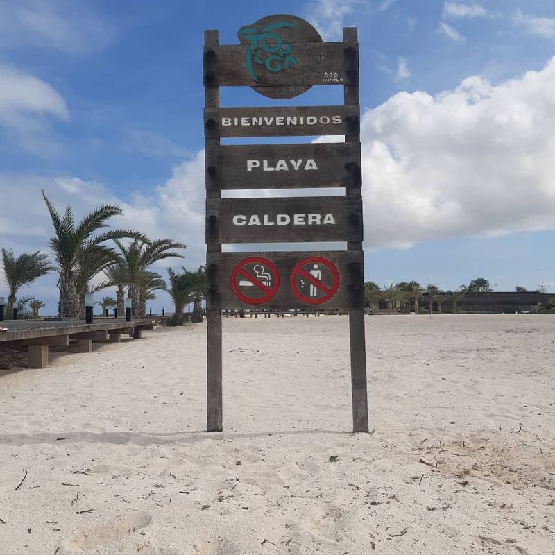 Letrero de bienvenida a Playa Caldera con palmeras y muelle de madera